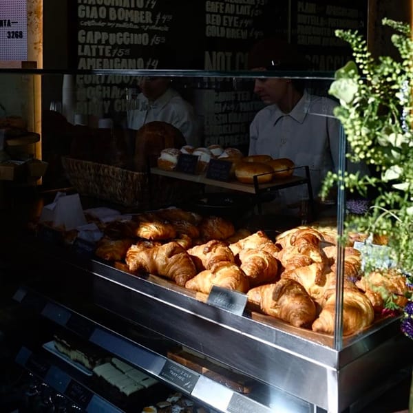 A cafe display case filled with golden croissants and pastries, with menu items visible in the background.