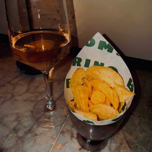 A glass of white wine next to a metal cup filled with Bomberino's potato chips on a marble table.