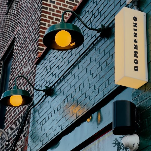 Bomberino cafe's exterior with a glowing sign and two green lamps on a brick wall.