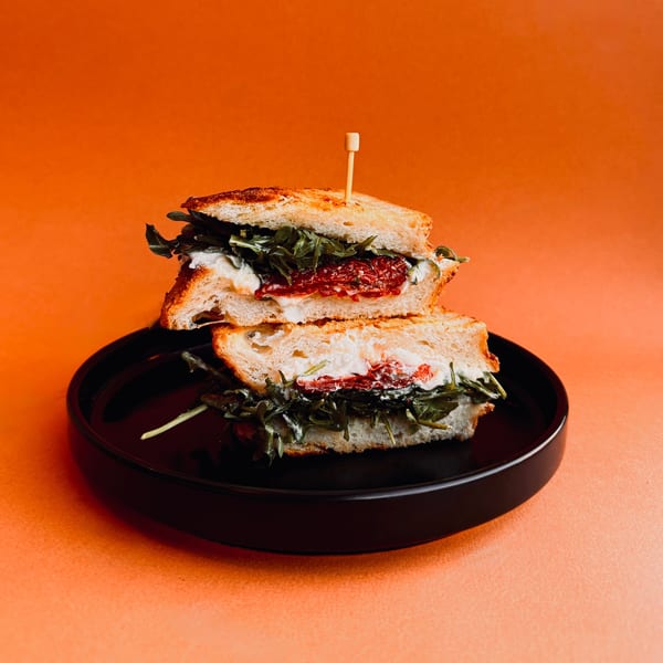 A Bomberino cafe sandwich with arugula, cheese, and sun-dried tomatoes on a black plate.