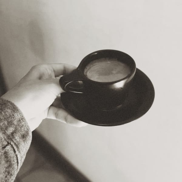 A hand holds a small black cup of espresso with a matching saucer in black and white.