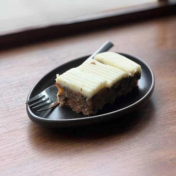 Two rectangular slices of Bomberino's cafe cake with white frosting and a fork on a black plate.