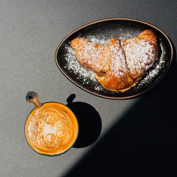 Overhead view of a Bomberino croissant dusted with powdered sugar and a latte with art.